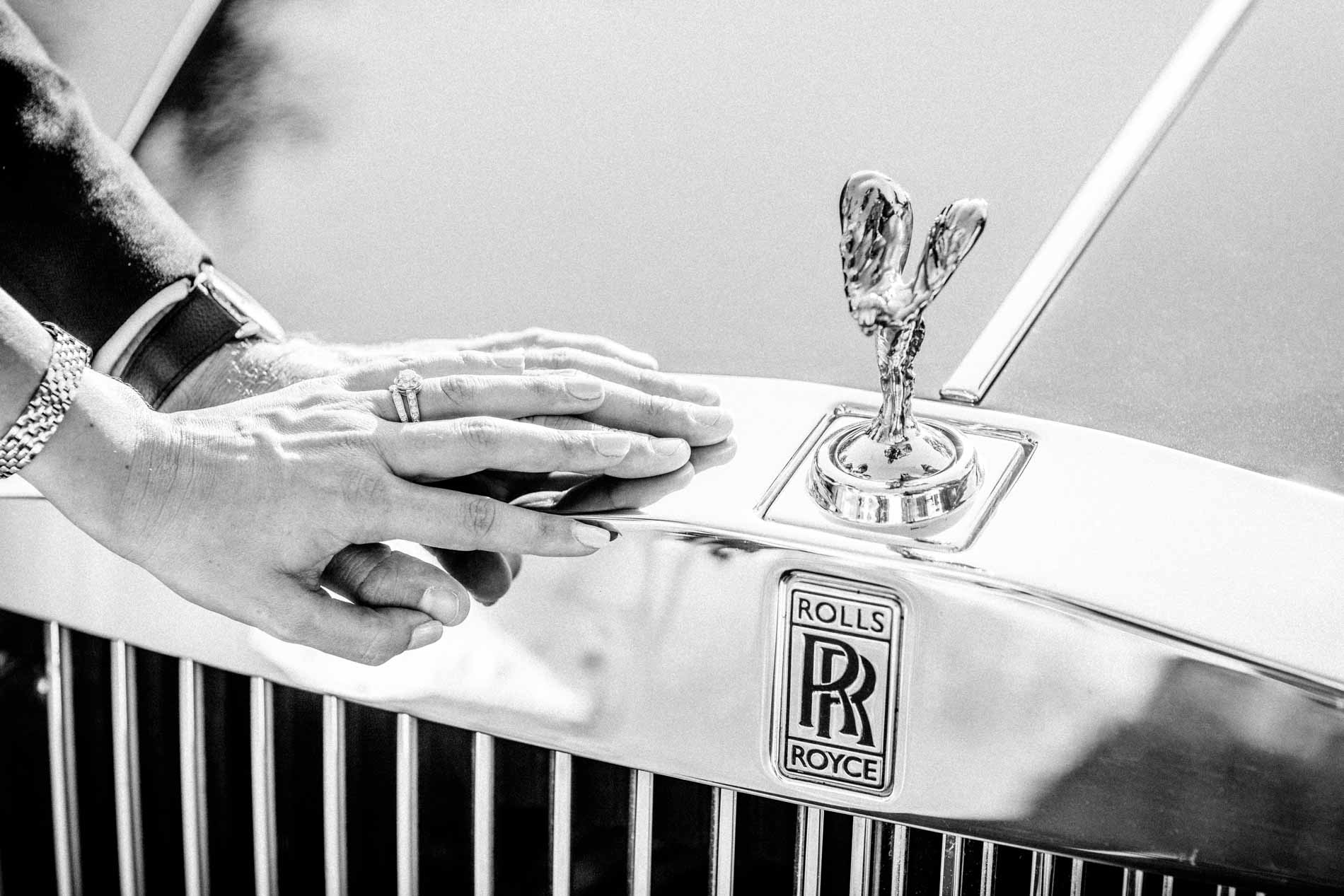 The couple's hands on the grille of a Rolls-Royce, in black and white