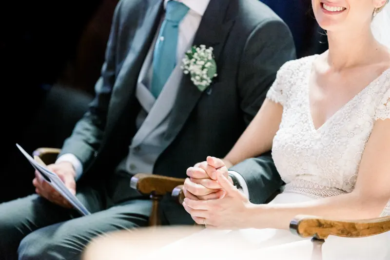 Mains jointes de la mariée assise près du marié pendant la messe