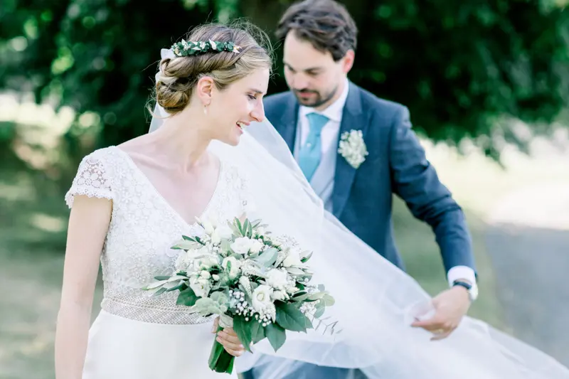 Le marié ajuste le voile de la mariée qui tient son bouquet blanc