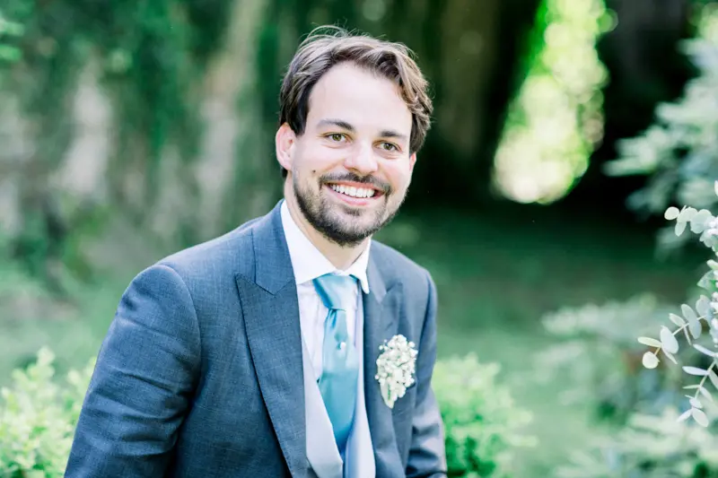 Portrait souriant du marié en costume gris-bleu dans un jardin normand