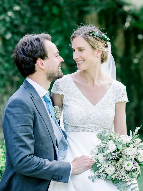 Mariés se regardant en souriant, bouquet blanc et feuillage vert