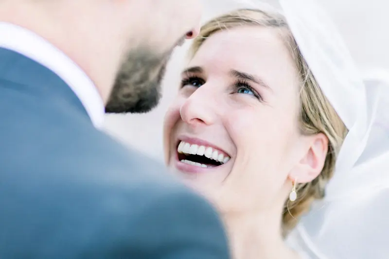 Mariée riant aux éclats, le visage tourné vers le marié sous le voile