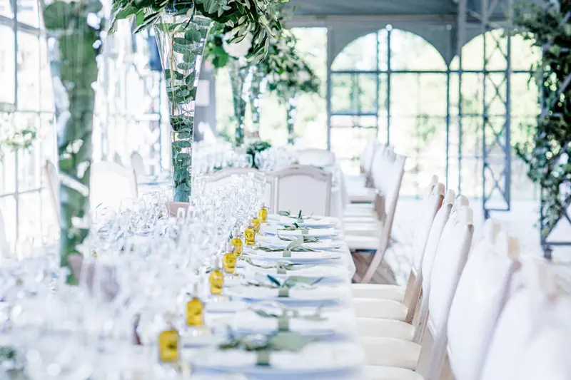 Longue table de mariage blanche avec bougies et verres dans l'orangerie