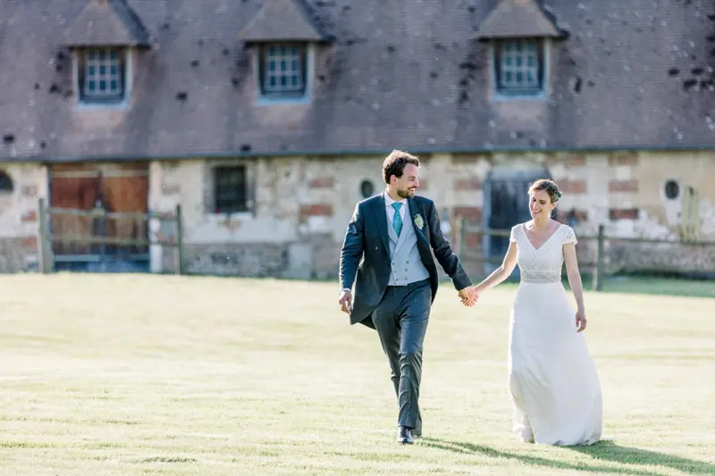 Mariés marchant main dans la main devant les communs du château