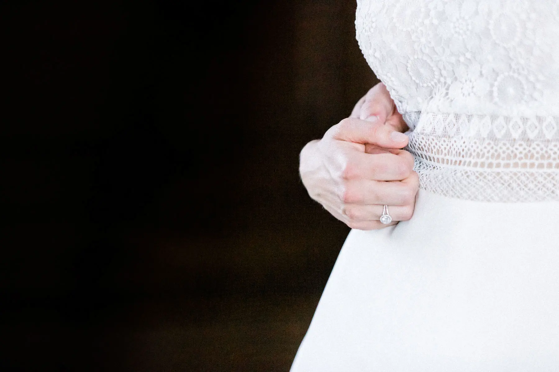 Main de la mariée posée sur sa robe en dentelle sur fond noir