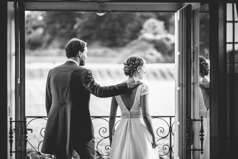 Mariés de dos sur le balcon regardant leurs invités, en noir et blanc