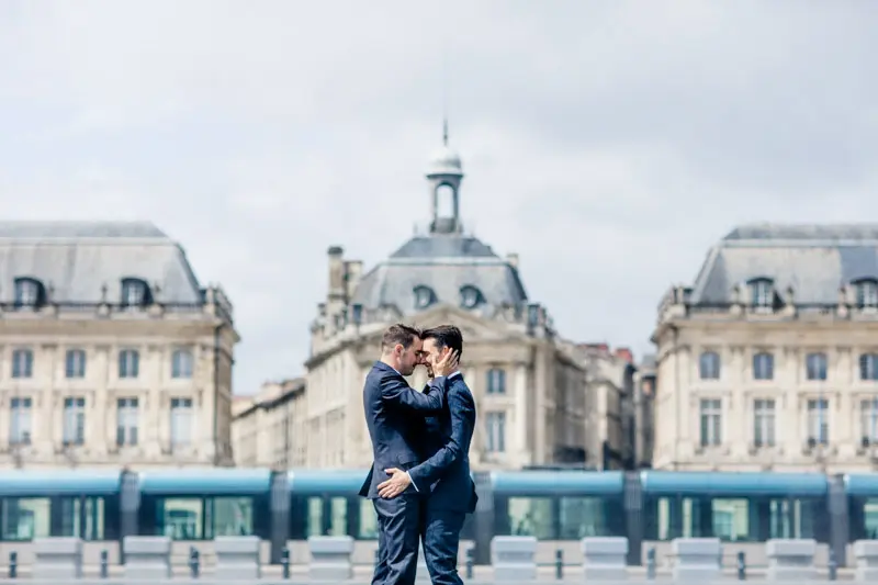 The two grooms embracing before Bordeaux's classical façades and a passing tram