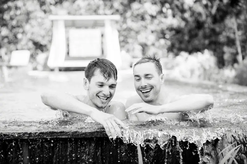 The two grooms-to-be laughing at the edge of the pool, in black and white