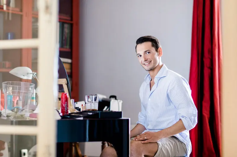 A groom in a shirt seated by the window while getting ready at the villa