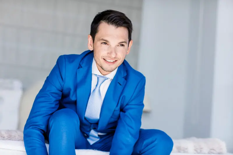 A groom in a royal blue suit sitting and smiling at Villa La Tosca