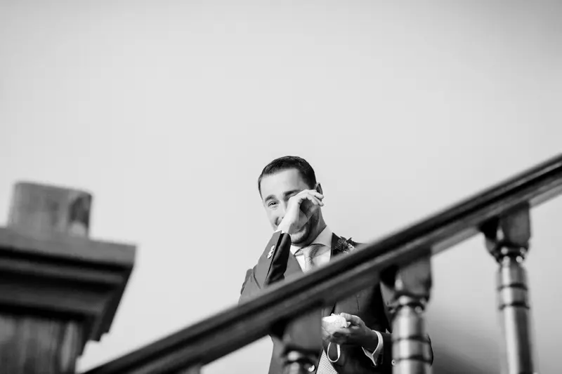 A groom overcome with emotion behind the banister before the first look, in black and white