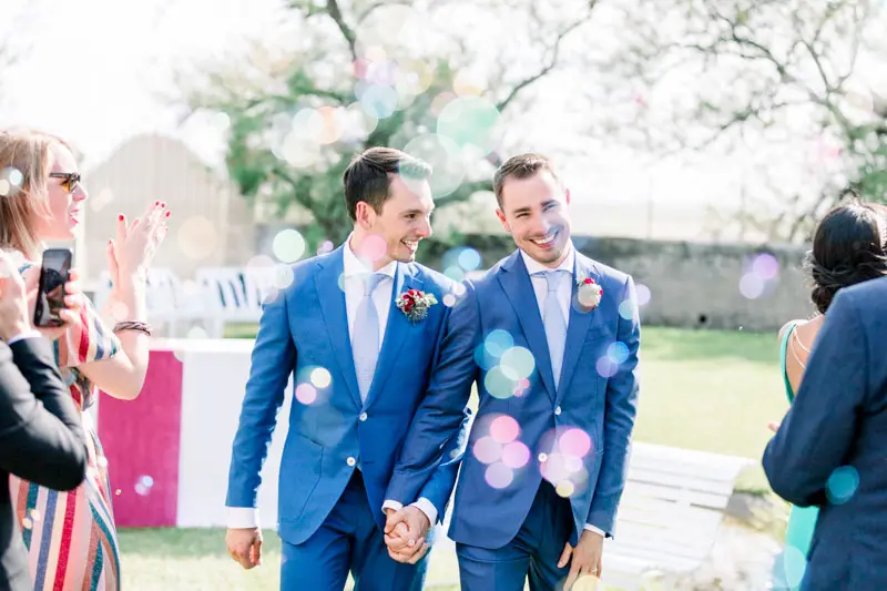 The two grooms leaving the ceremony hand in hand under soap bubbles