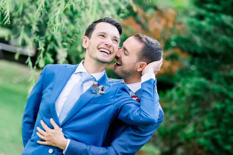 The grooms bursting into laughter in each other's arms in the garden
