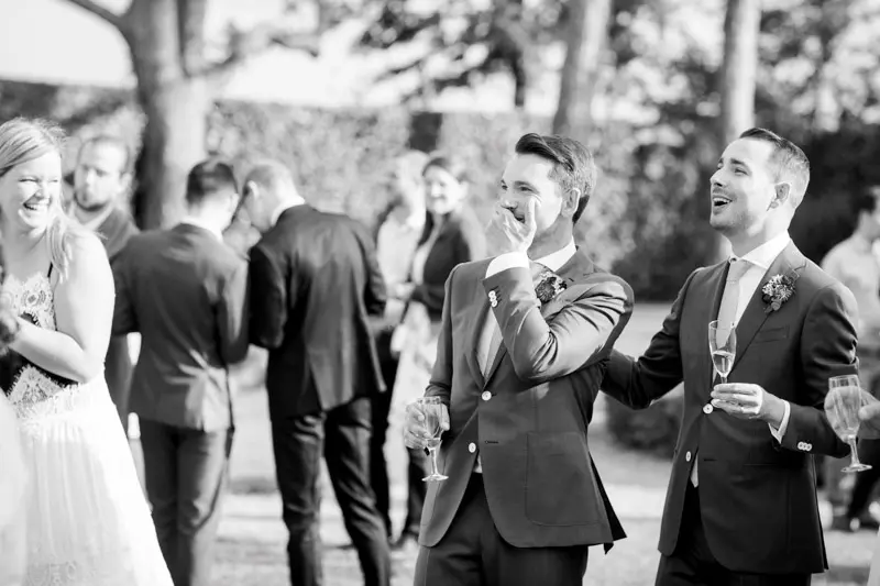 The grooms laughing with their guests during the surprise drinks, in black and white