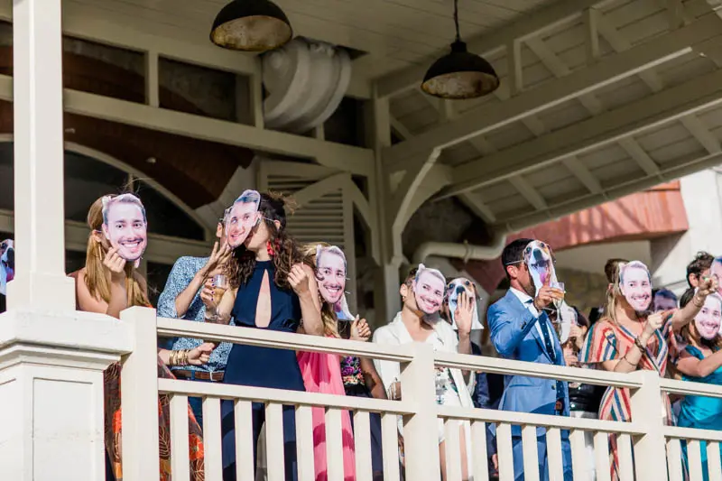 Guests wearing masks of the grooms' faces on the veranda for the surprise