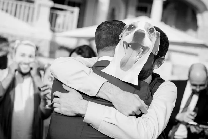 A groom hugging a guest in a dog mask, in black and white