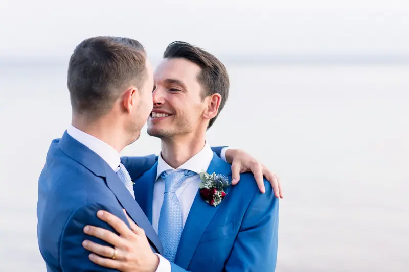 The two smiling grooms forehead to forehead on the shore of Arcachon Bay