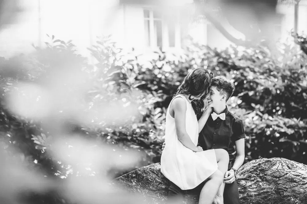 The couple sharing a moment on a log amid the greenery, in black and white