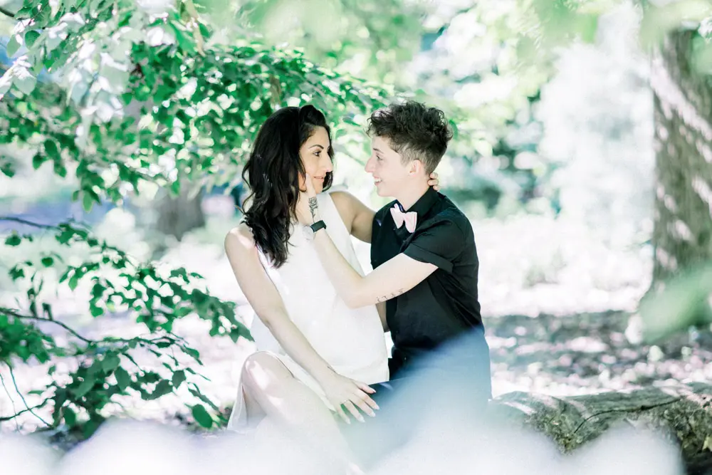 The couple sitting by the water, exchanging glances beneath the trees