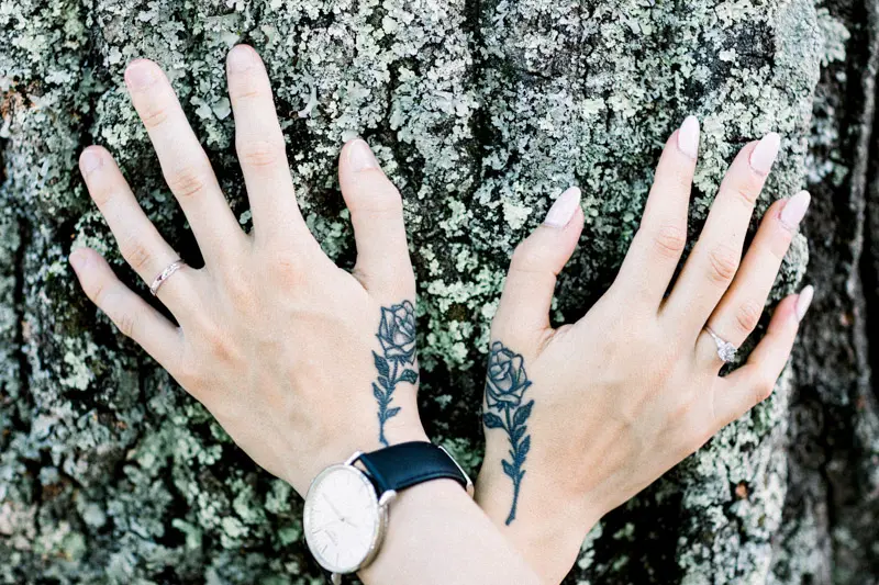 Two tattooed hands resting on lichen-covered tree bark