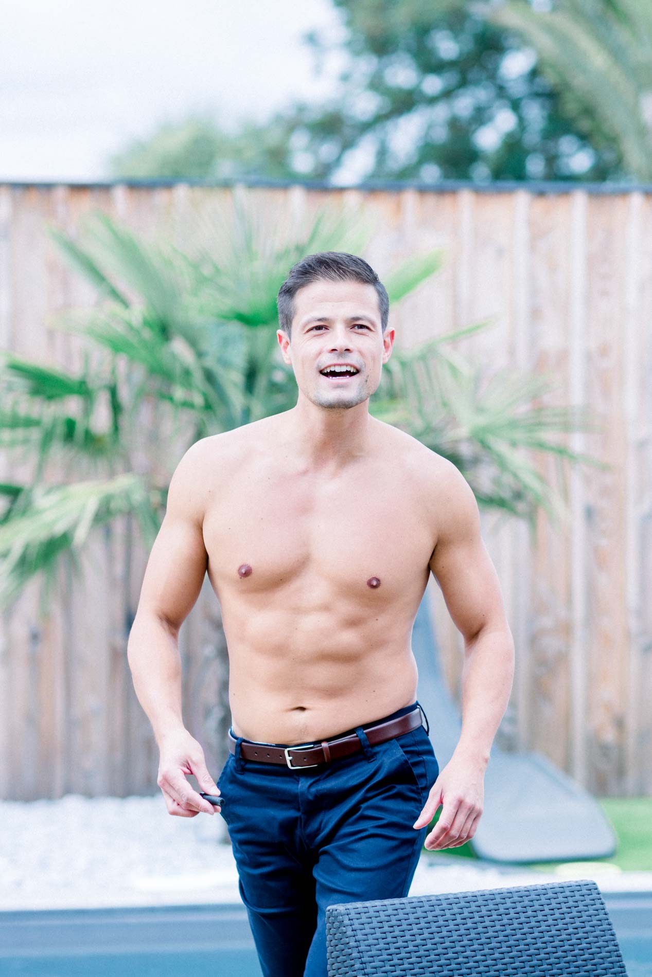 Groom smiling shirtless by the pool before getting dressed