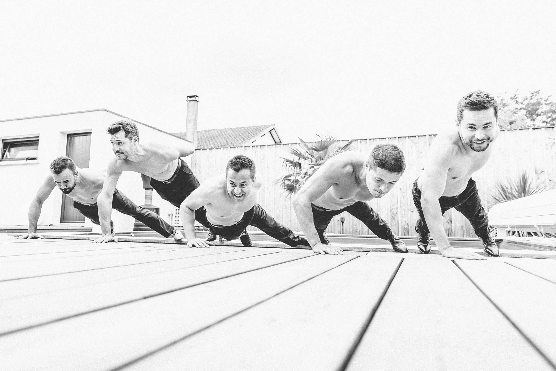 Groom and his friends doing push-ups shirtless on a wooden deck