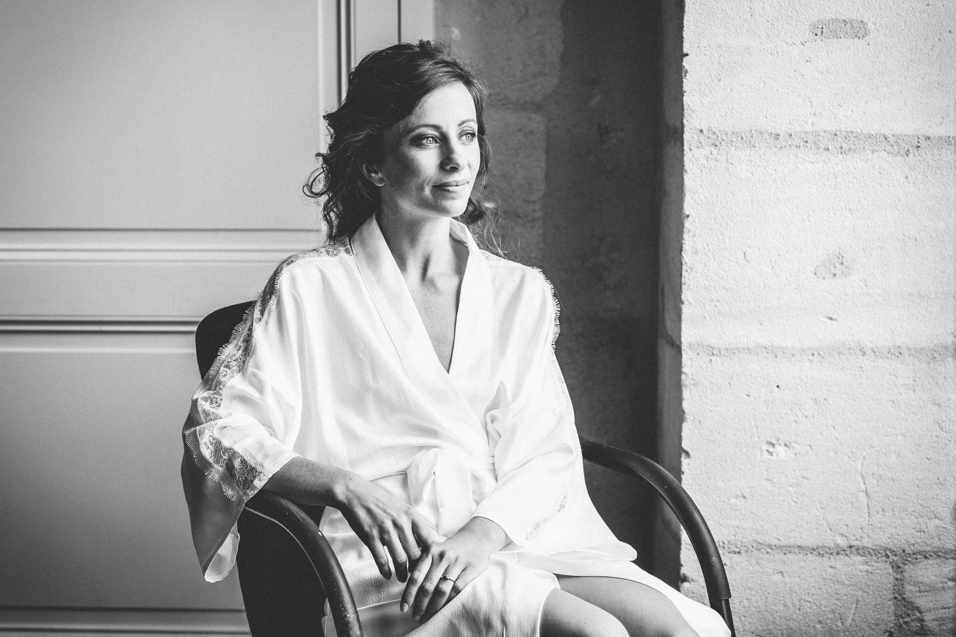 Bride in her robe sitting by a window, in black and white