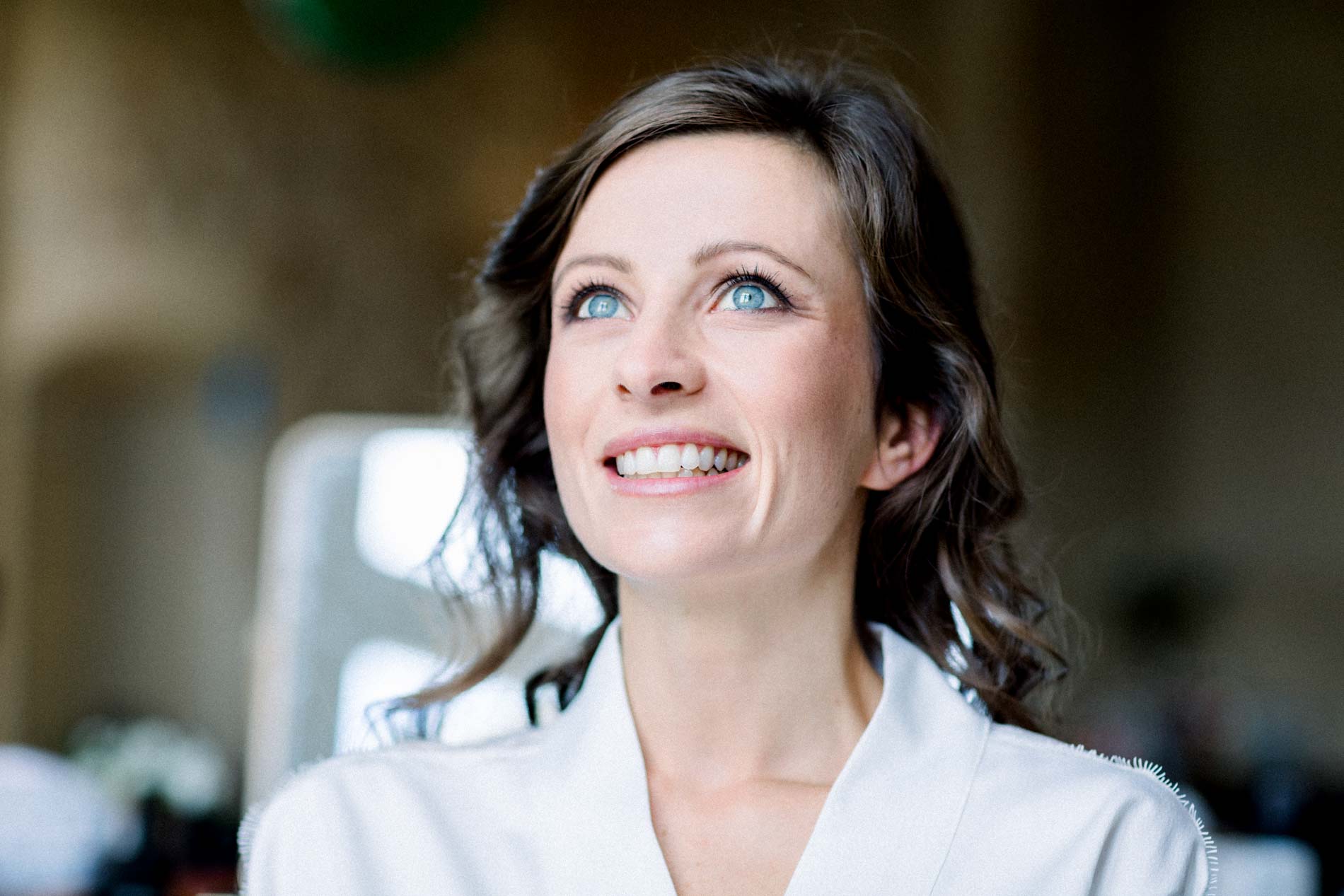 Portrait of the smiling bride in a white robe while getting ready