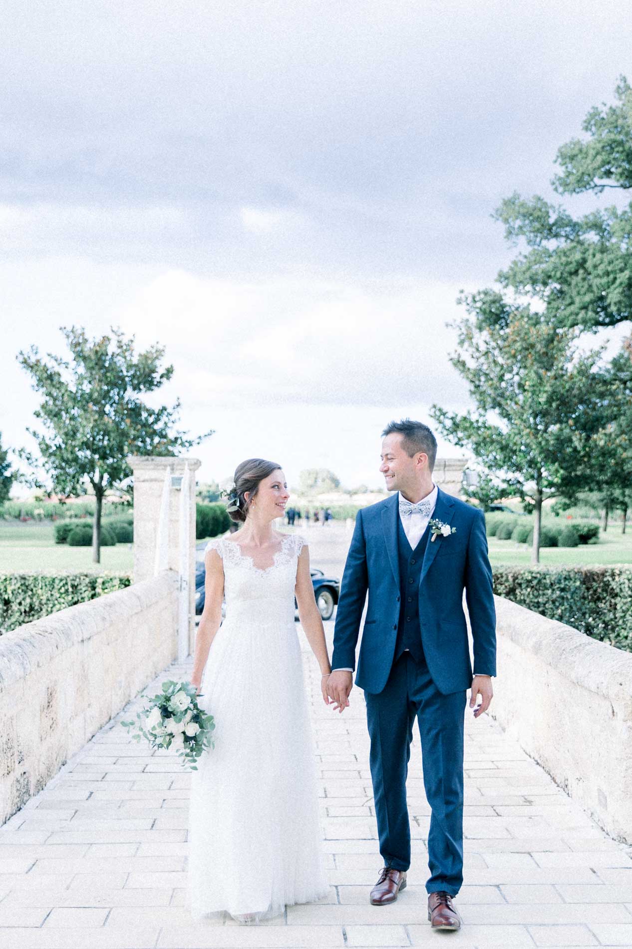 The newlyweds walking towards the camera on the stone bridge of Château d'Agassac