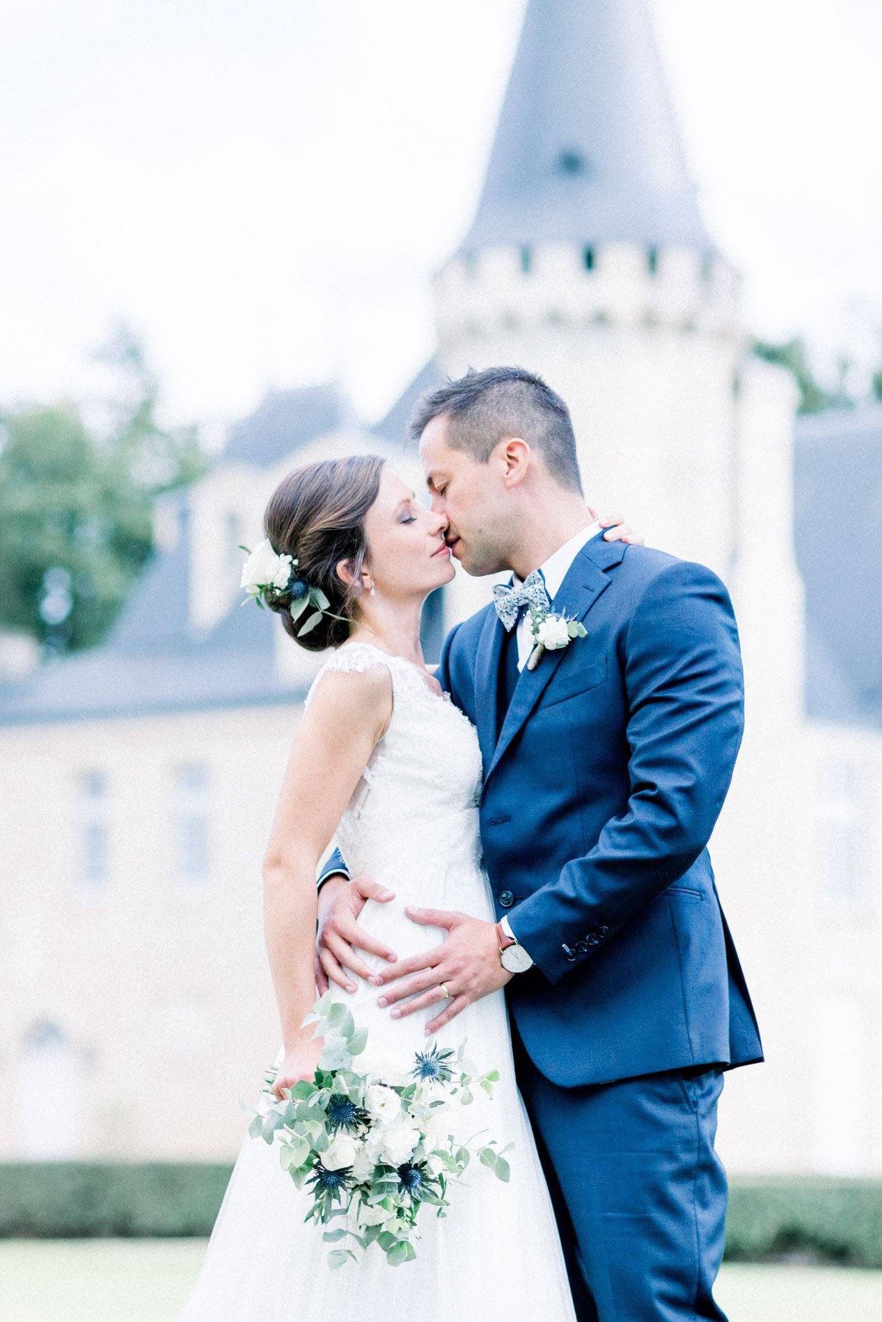 The bride and groom kissing, hand on her waist, before a château turret