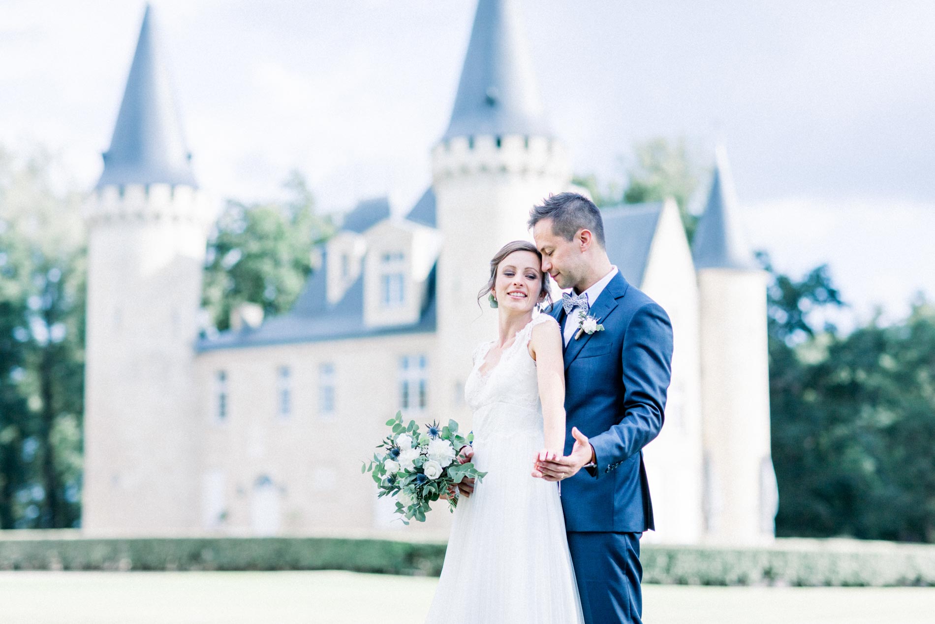 The couple posing in front of Château d'Agassac, white bouquet in hand