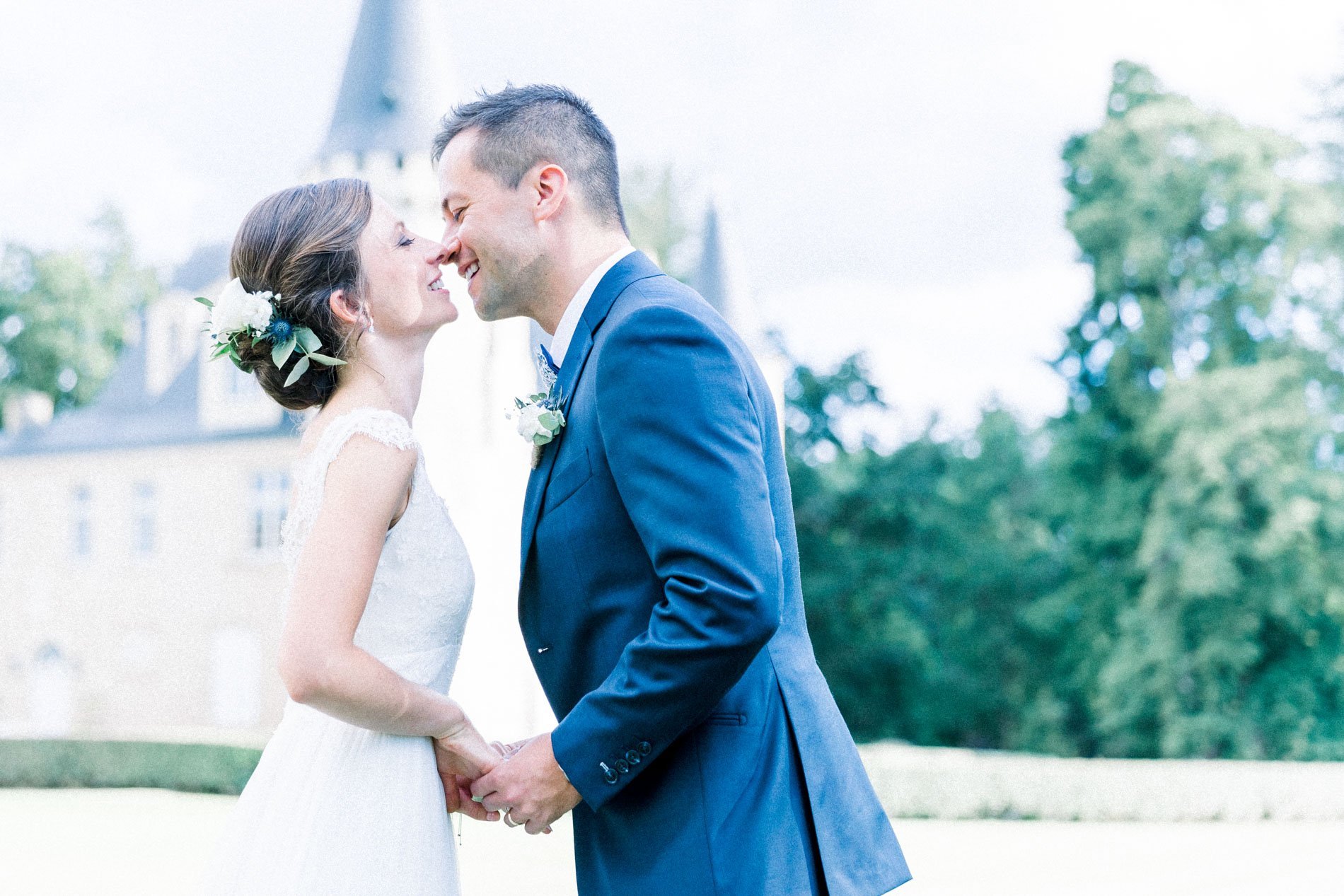 Bride and groom forehead to forehead, holding hands in front of the château