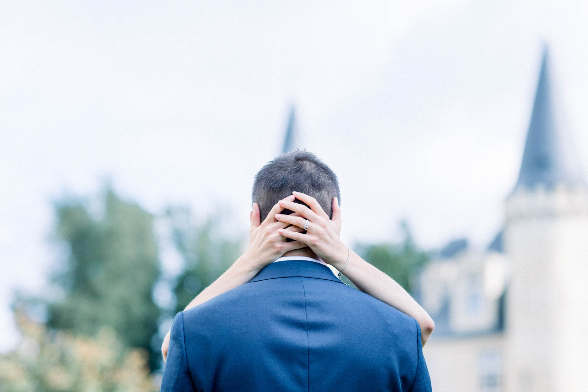 The bride's hands resting on the back of the groom's neck, château behind