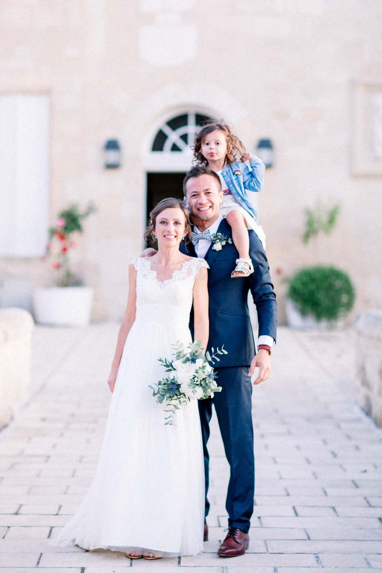 The couple posing with a little girl on the groom's shoulders