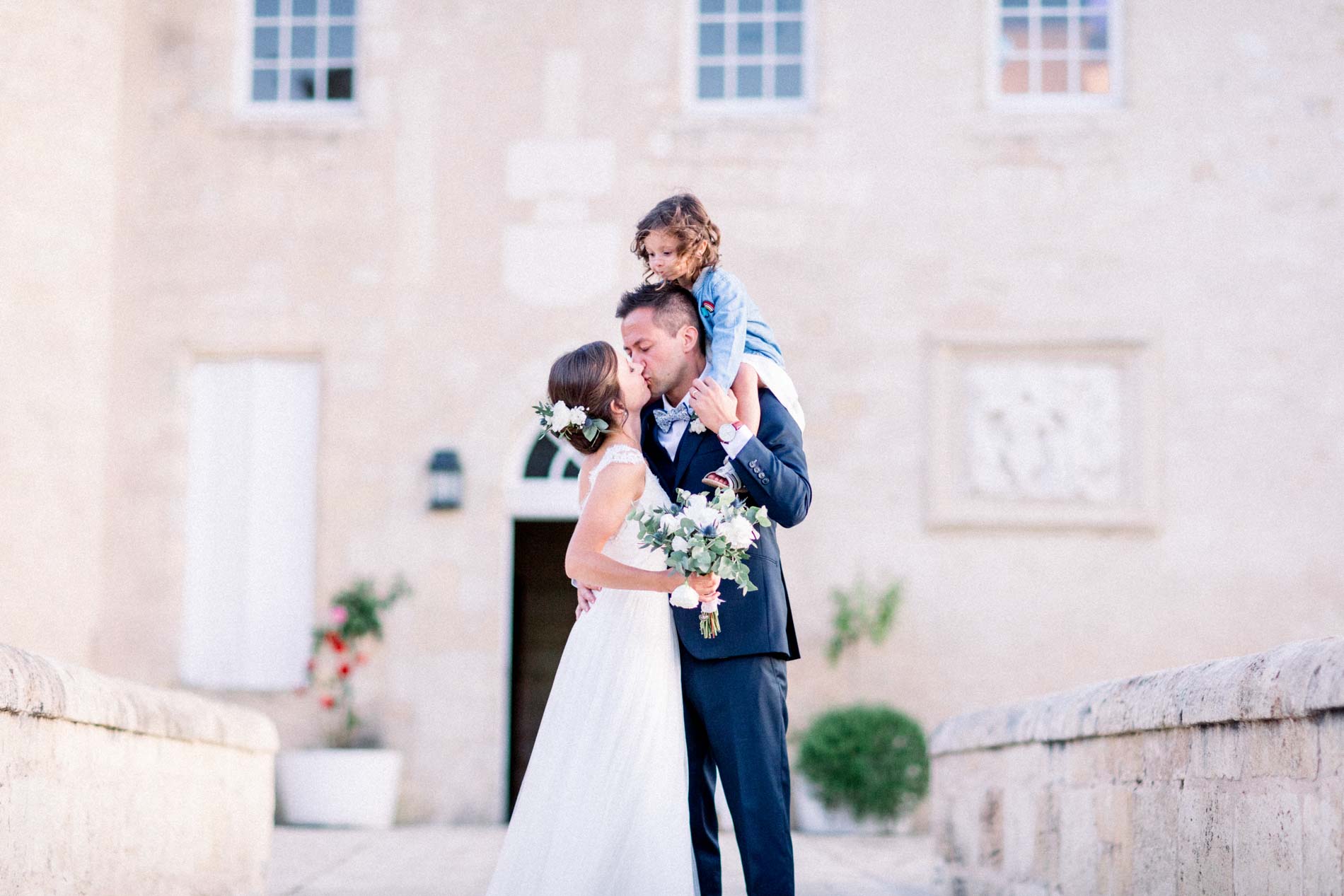 The bride kissing the groom as he carries a little girl on his shoulders