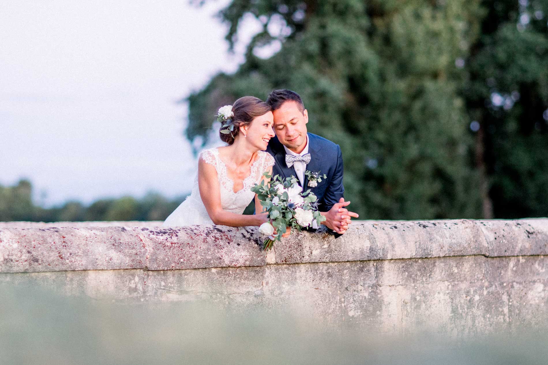 The couple leaning on a low stone wall at sunset