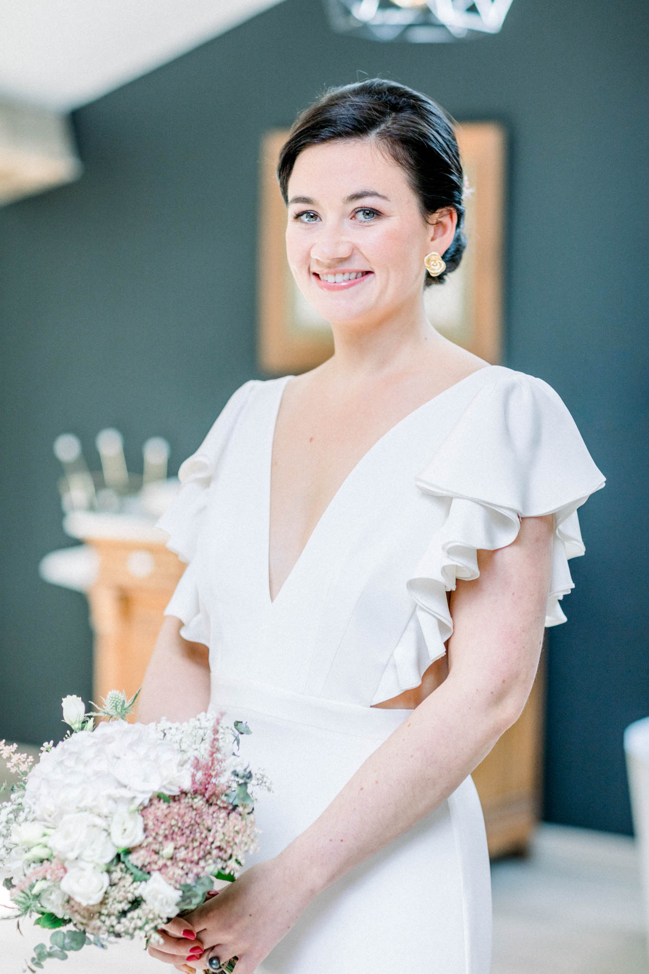 The bride in a ruffled gown holding her bouquet against a teal wall