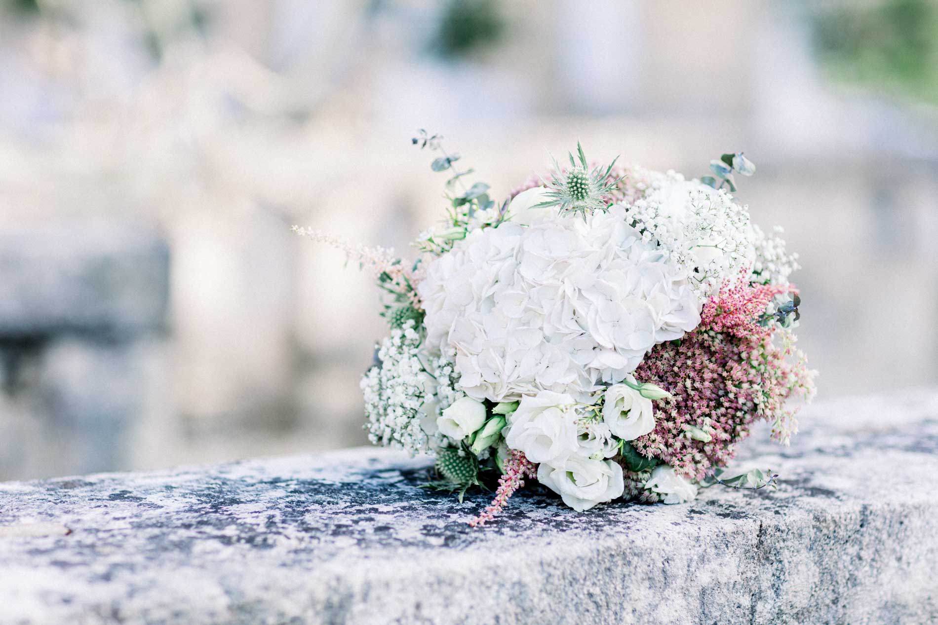 White and dusty pink bridal bouquet resting on a stone ledge