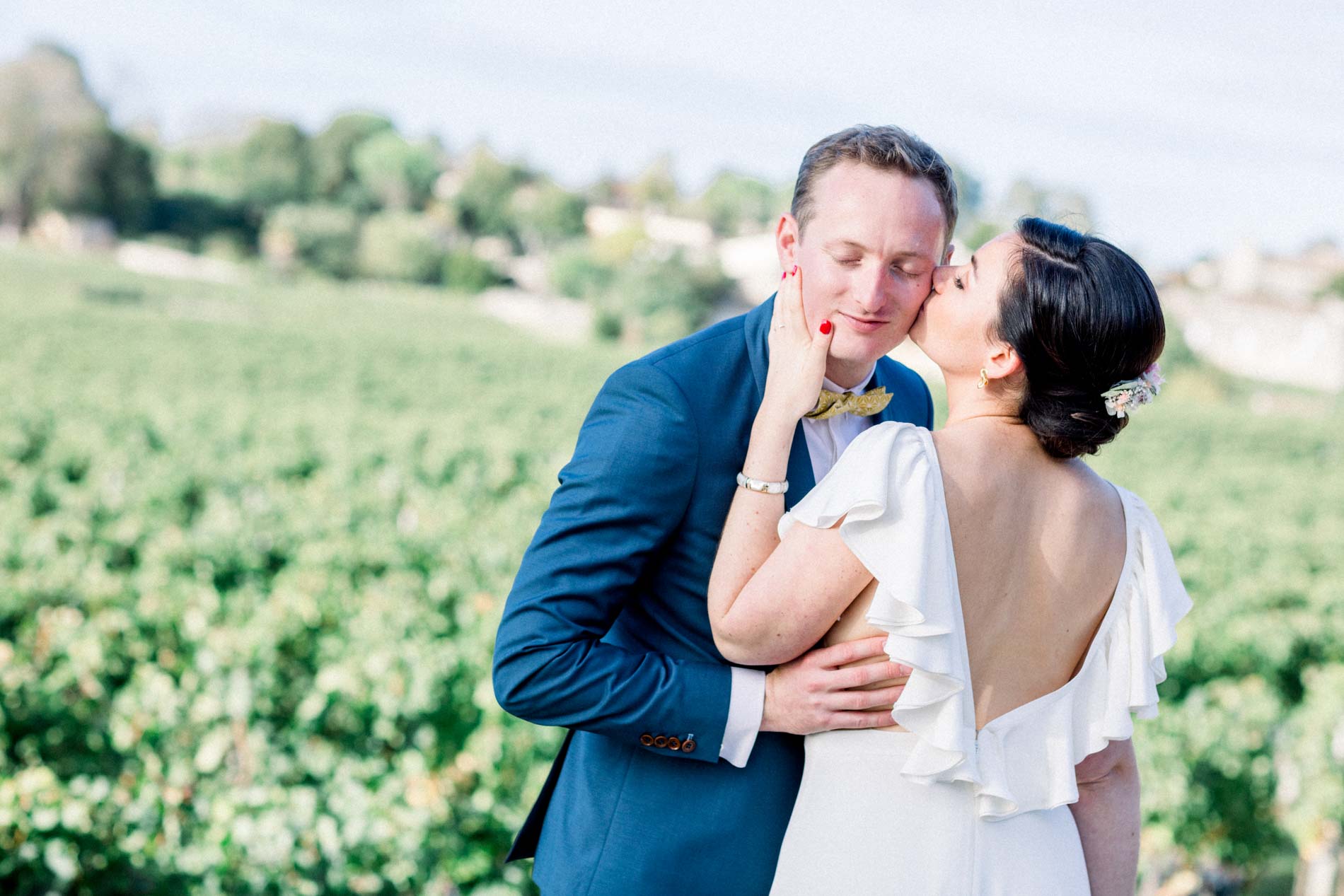 The bride in a backless gown kissing the groom's cheek in the vines