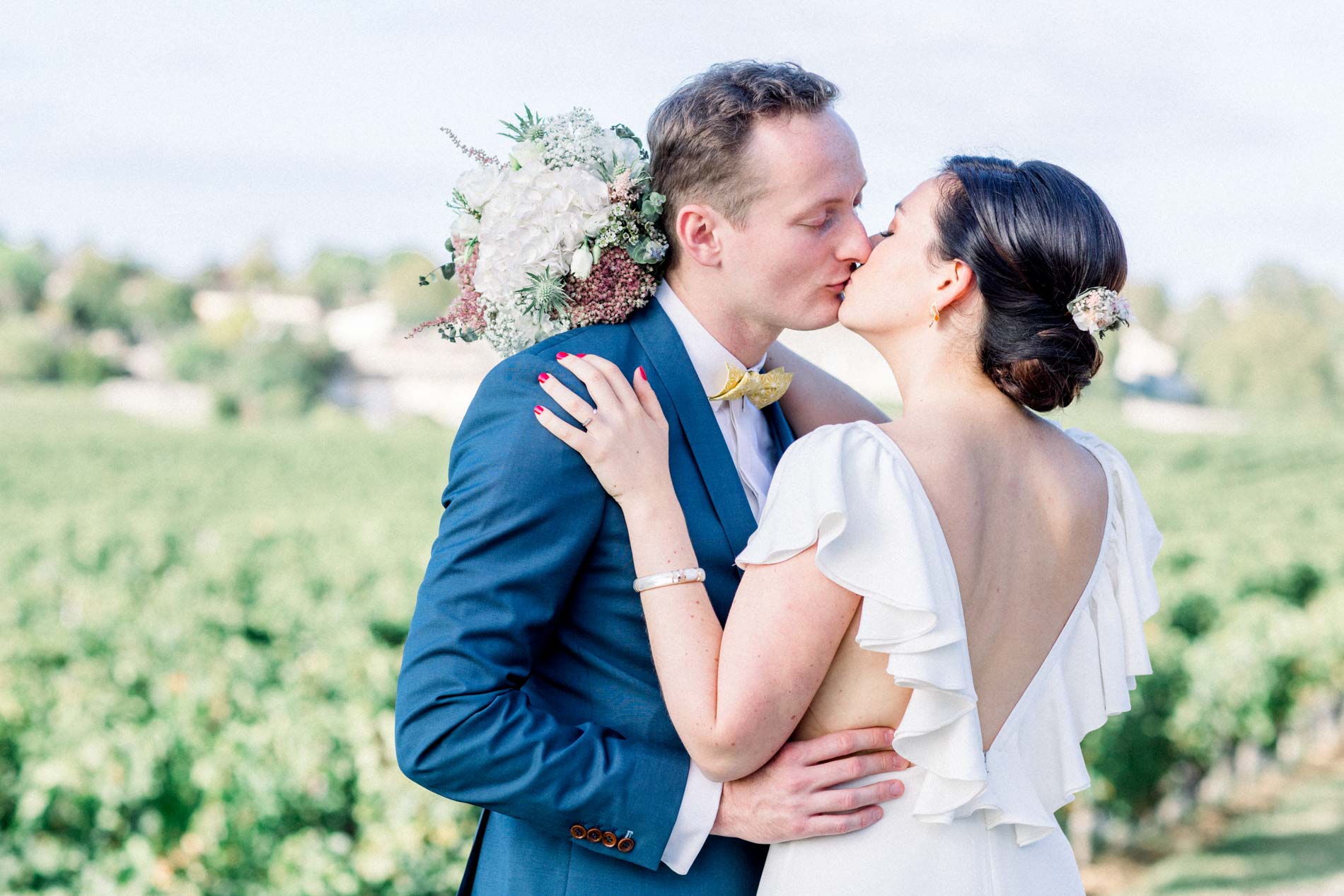 The couple kissing among the vines, bouquet in hand