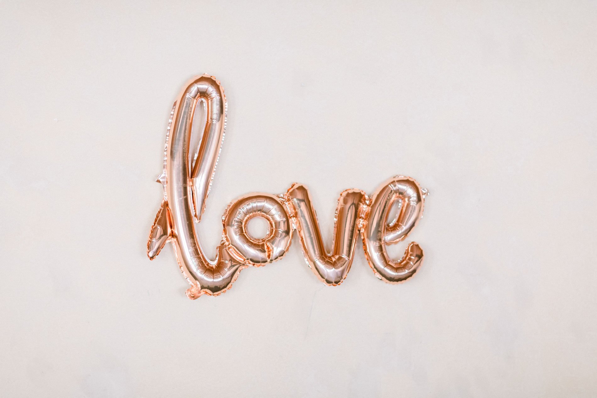 Rose gold "love" balloon on a white wall as wedding decor