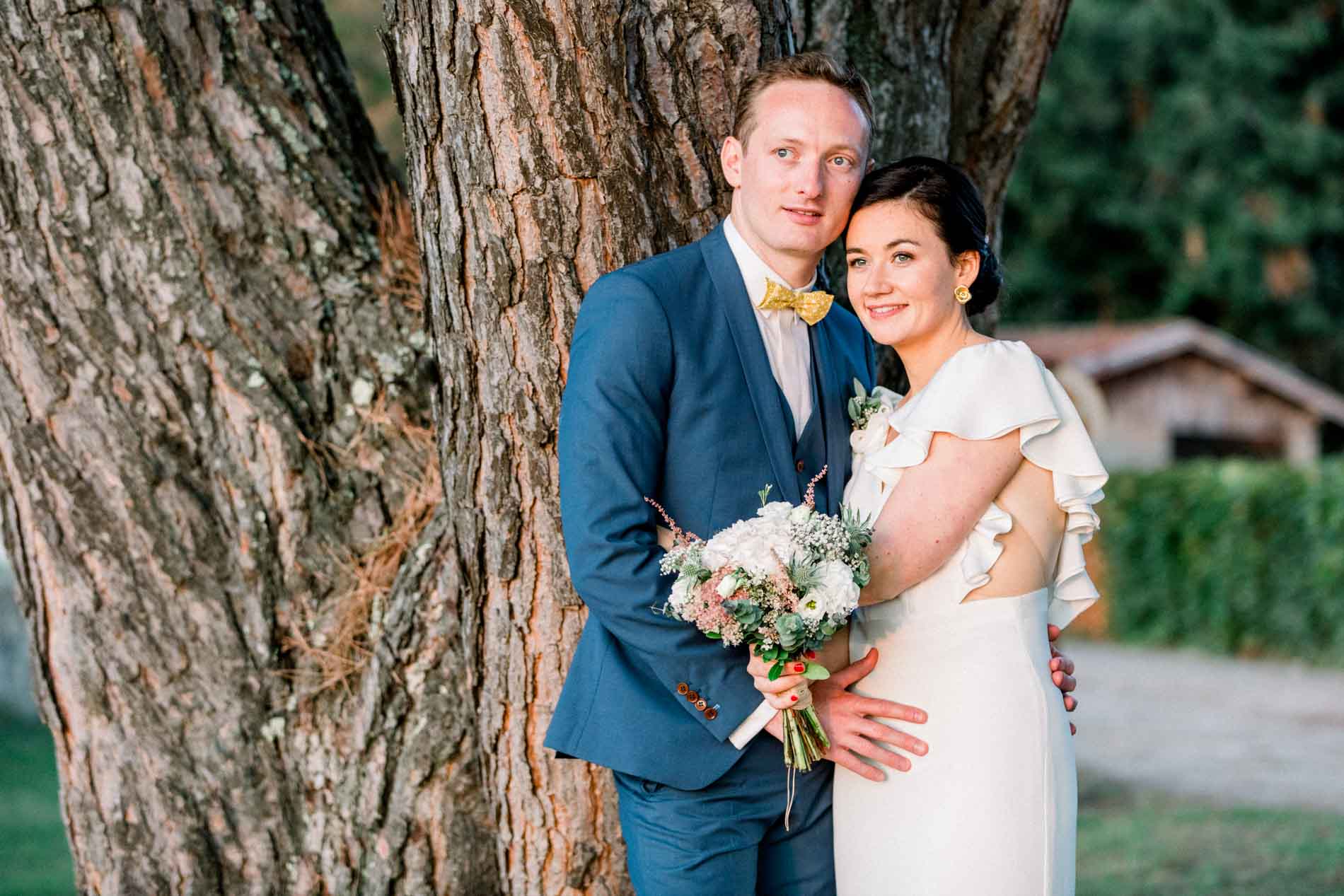 The couple embracing against an old tree trunk at sunset