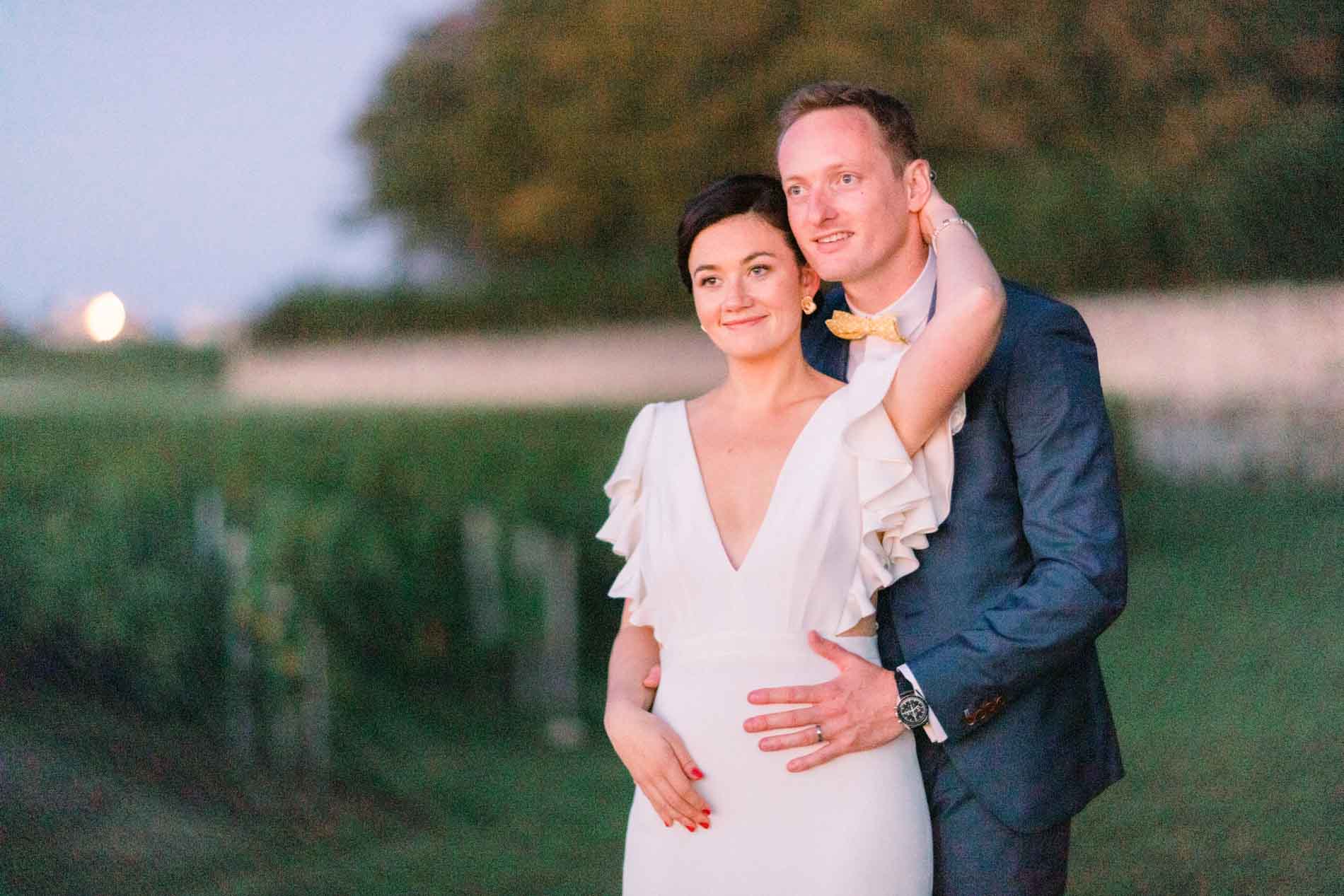 The bride leaning against the groom at dusk in the vineyard