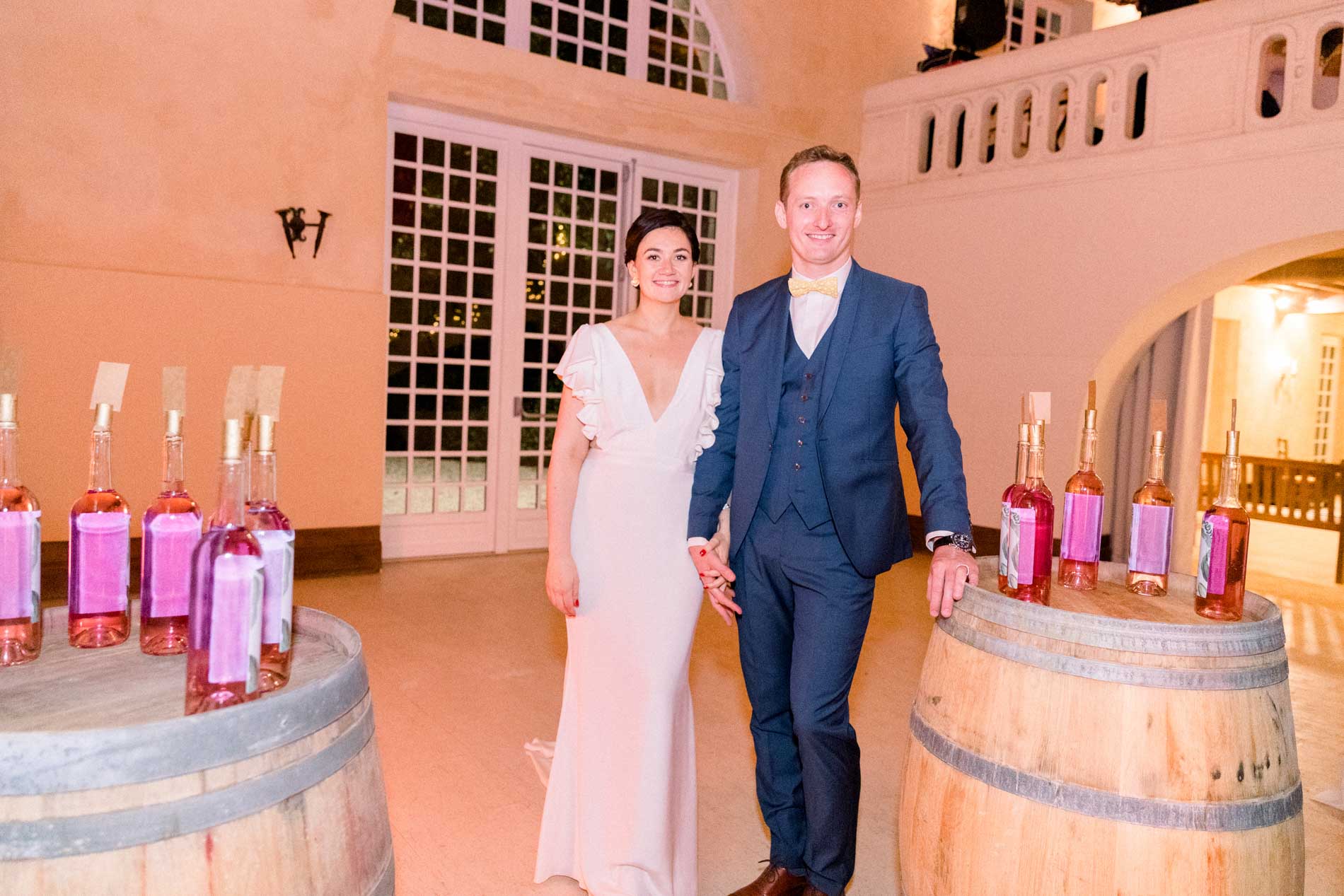 The bride and groom between two barrels topped with bottles of rosé