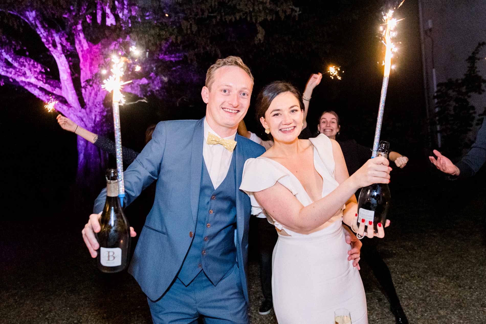 The bride and groom raising champagne bottles topped with sparklers