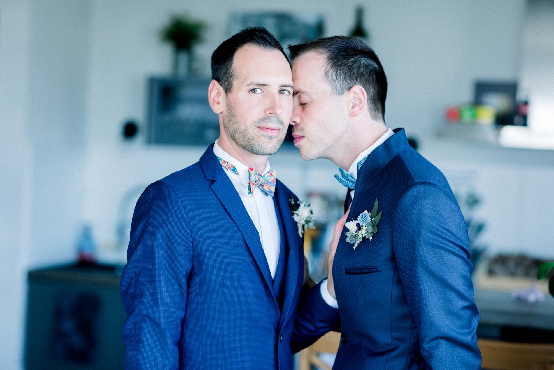 Les deux mariés en costume bleu, joue contre joue, dans la maison