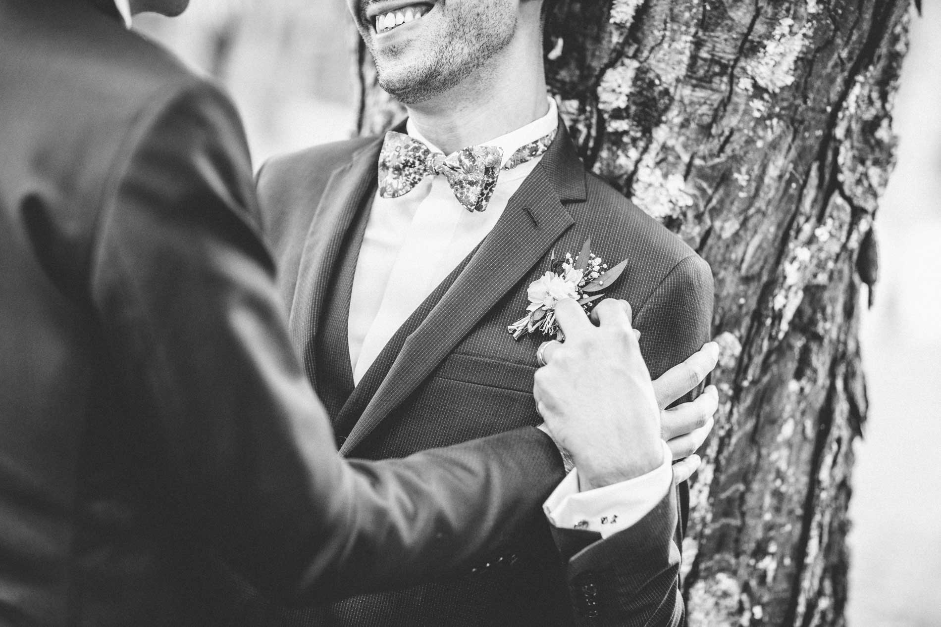 Détail d'une boutonnière et main sur la veste, contre un arbre, en noir et blanc