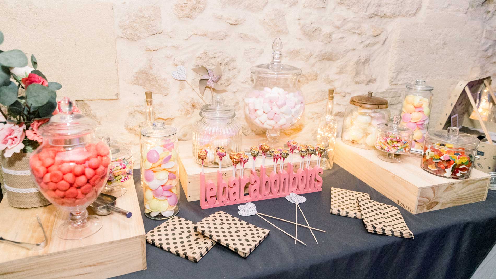 Bar à bonbons coloré devant un mur en pierre, bocaux et dragées