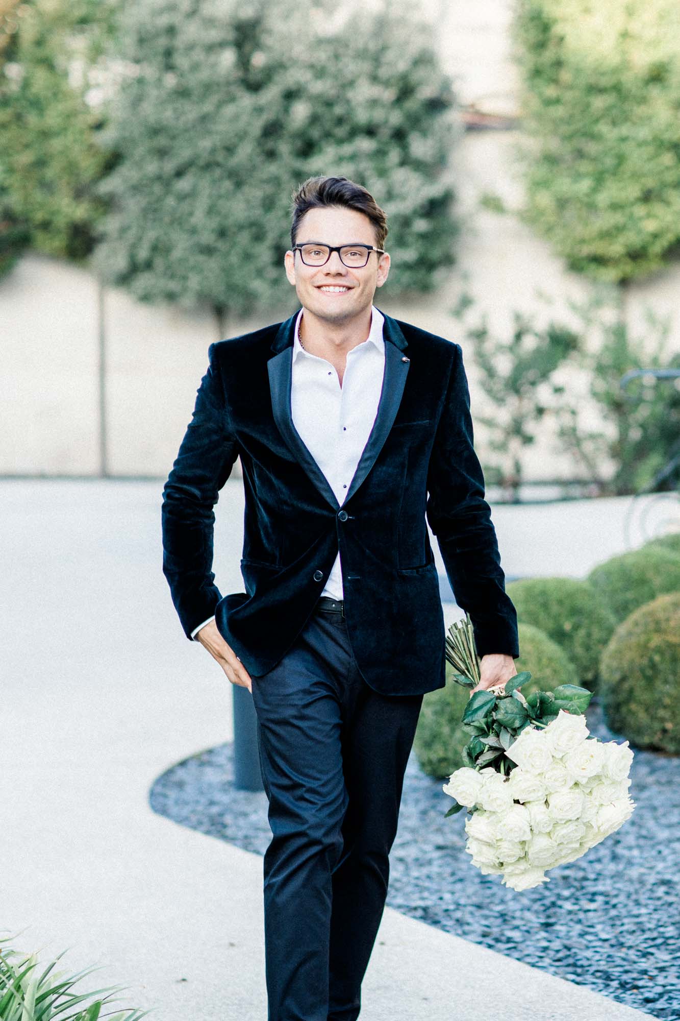 The man in a velvet suit walking through the garden with white roses in hand