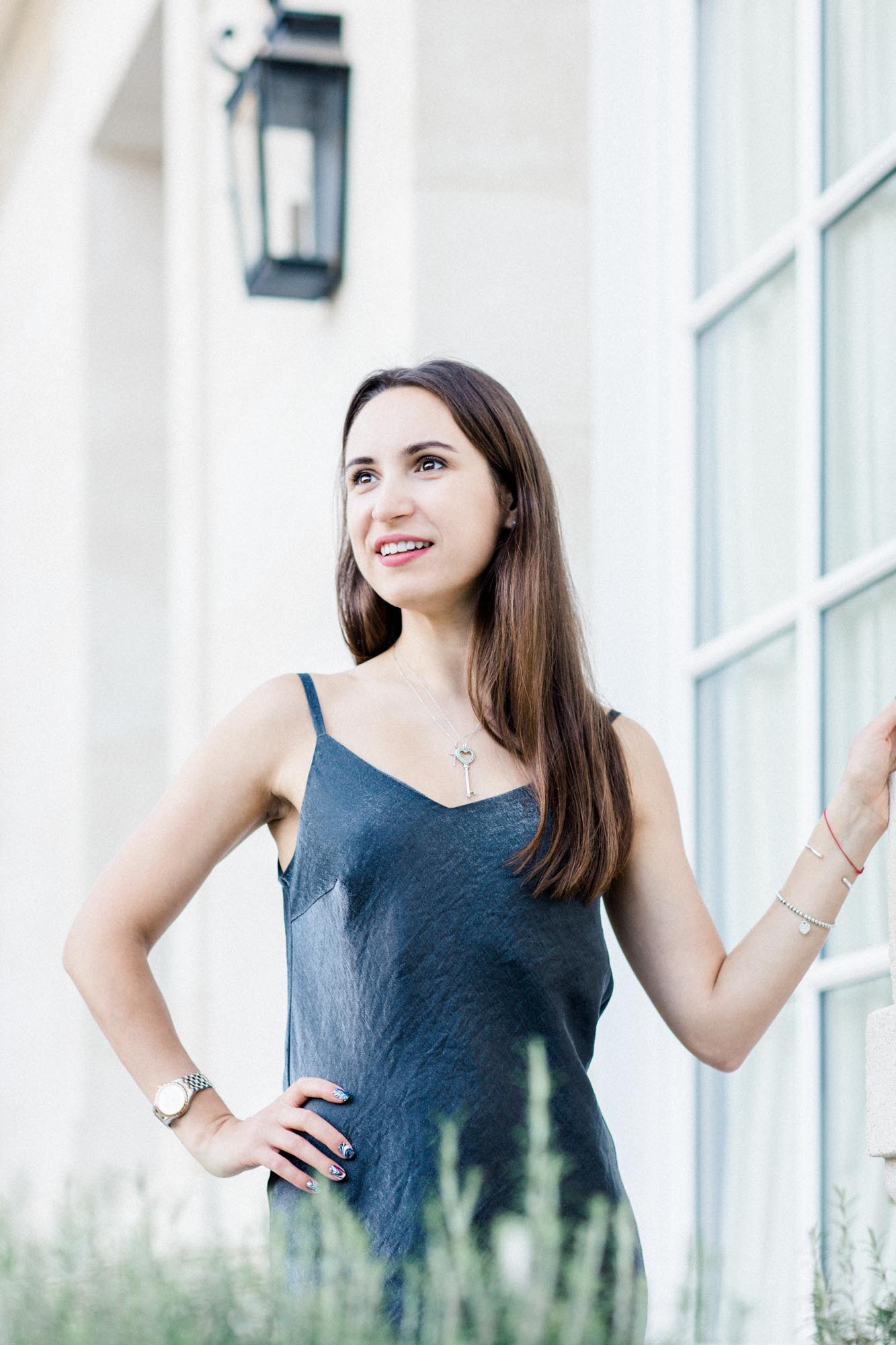 Young woman in a blue slip dress posing by a stone French window
